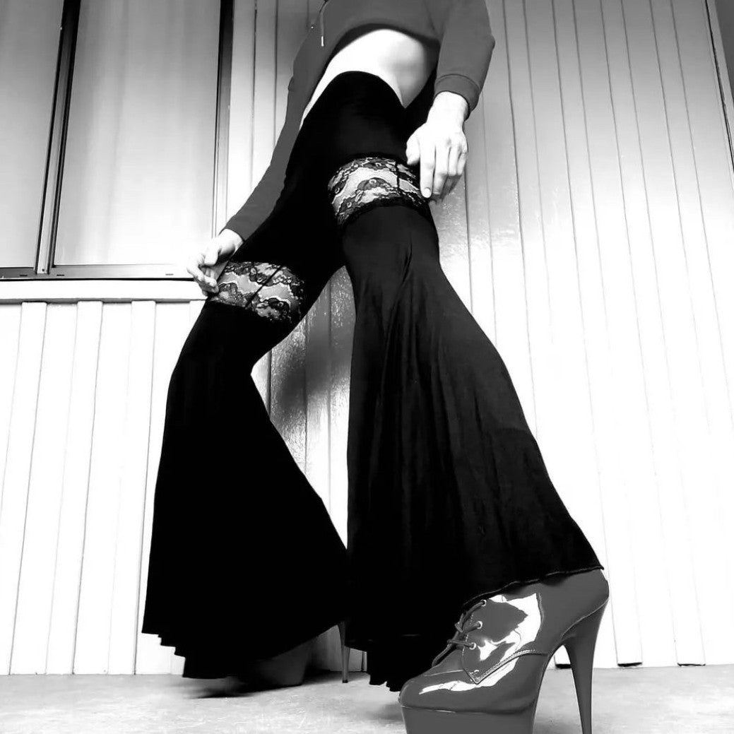 Man wearing black flared pants and high heels, standing in a confident pose indoors.