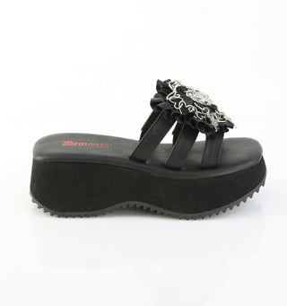 Side view of black Demonia flip-16 platform sandal with thick wedge sole, triple black straps, ruffled trim, and silver gothic heart and cross charms.