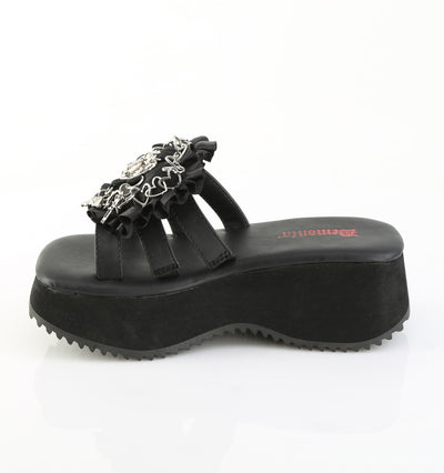 Side view of black Demonia flip-16 platform sandal with ruffled strap, silver gothic charms, and triple black straps over a chunky wedge sole.