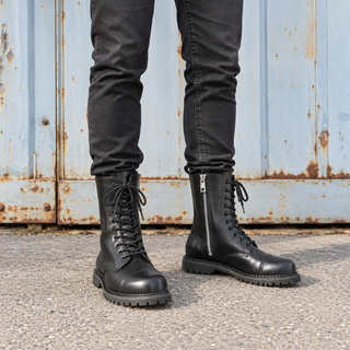 Model wearing black Demonia RIOT-10 leather combat boots with black jeans, showing the lace-up fronts and silver side zip.