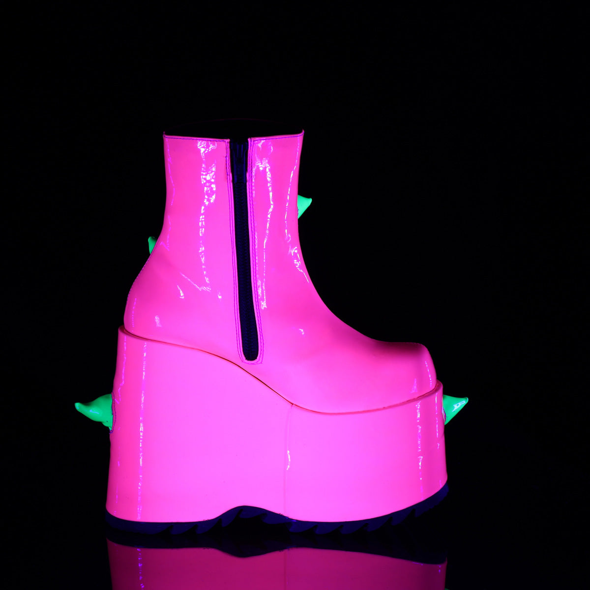 Inner side view of the Demonia Slay-77 neon pink platform boot featuring a black zipper, exaggerated wedge heel, and hints of green spikes peeking from the other side, shown under blacklight.