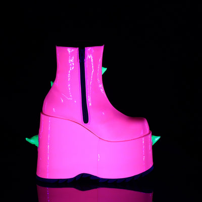Inner side view of the Demonia Slay-77 neon pink platform boot featuring a black zipper, exaggerated wedge heel, and hints of green spikes peeking from the other side, shown under blacklight.