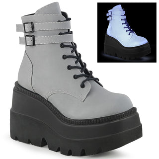 A pair of grey platform boots (Demonia Shaker-52) with a lace-up front, double ankle buckles, and a chunky black sole. The upper has a reflective finish that lights up in the dark.