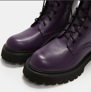 lose-up of purple vegan leather combat boots showing black laces and chunky treaded soles.