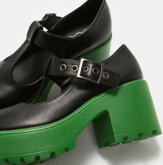 Close-up of black Mary Jane platform shoes featuring chunky green soles, T-strap buckle, and textured tread.